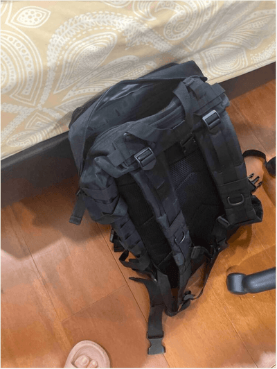 Black tactical backpack on a wooden floor with a patterned rug