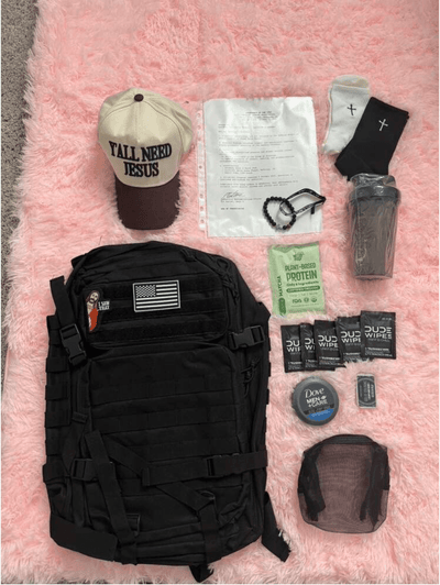 Black backpack with various items including a cap, paper, and snacks on a pink surface