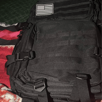 Black tactical backpack with American flag patch on a textured surface