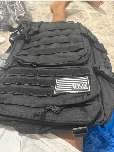Black tactical backpack with American flag patch held by a person.