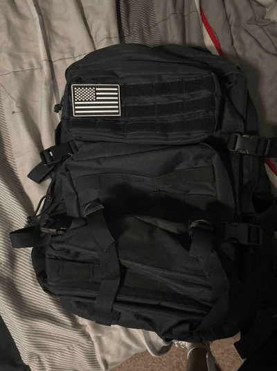 Black tactical backpack with American flag patch on a bed