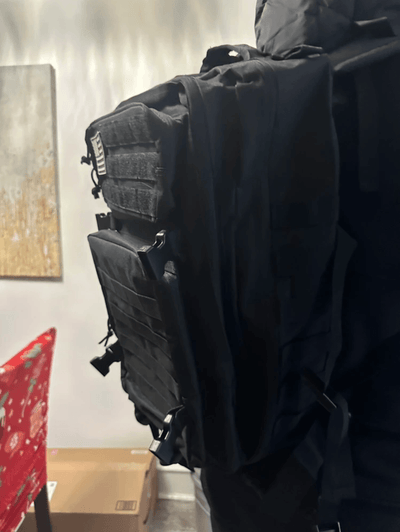Black tactical backpack with visible straps and equipment on a plain background