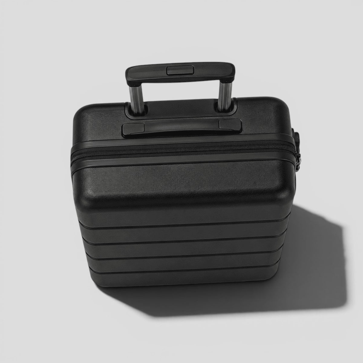 Top down view of black matte hardshell carry on luggage showing perimeter zipper, side carry handle, and spinner wheel base
