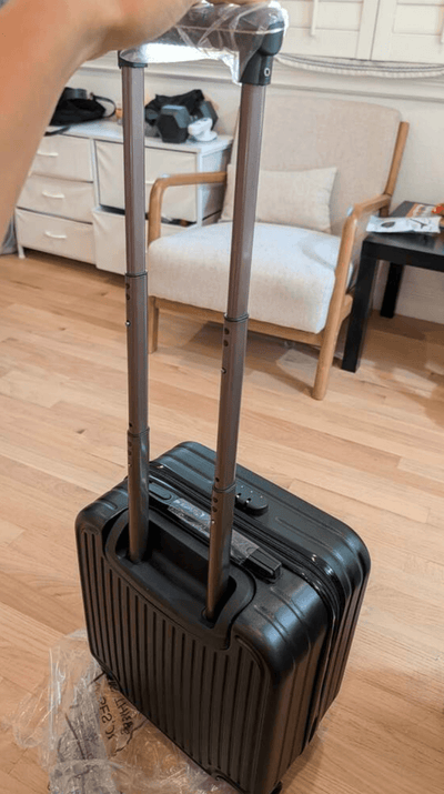 Black suitcase with a handle on a wooden floor in a room.